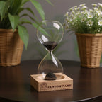 Reloj de arena personalizado con nombre y base de madera, diseño creativo con efecto natural en espejo, ideal para regalo de boda, fiesta y decoración elegante.